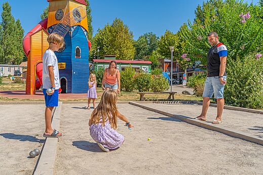 Familia jugando a la petanca en la cancha, con zona de juegos en el camping CAPFUN Temps Libre en BOUGE CHAMBALUD (38).
