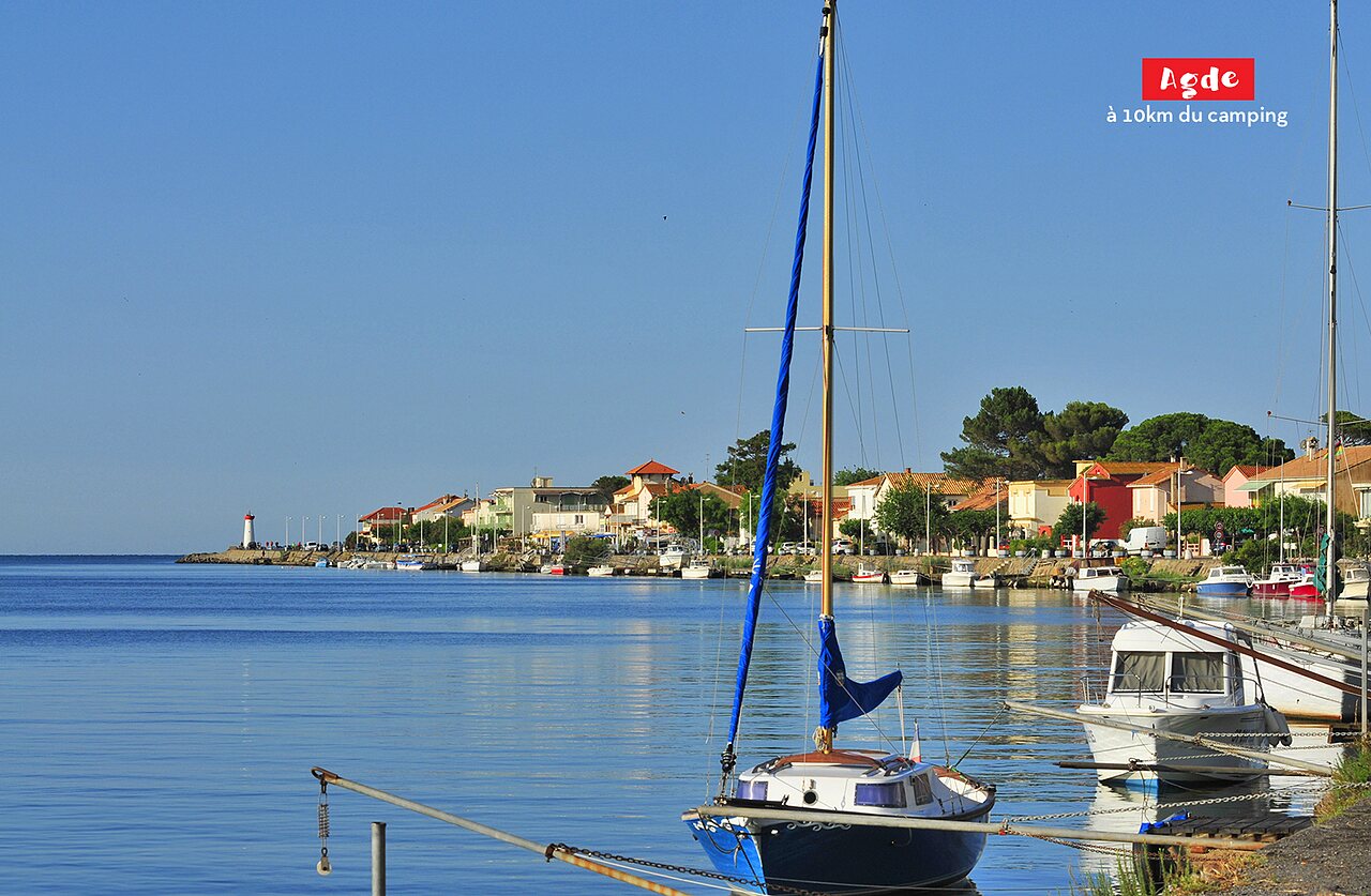 Puerto de Agde con veleros, casas coloridas y faro, cerca de Marseillan Plage.