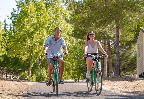 Pareja en bicicleta por camino arbolado en camping CLICOCHIC Plage des Tonnelles.