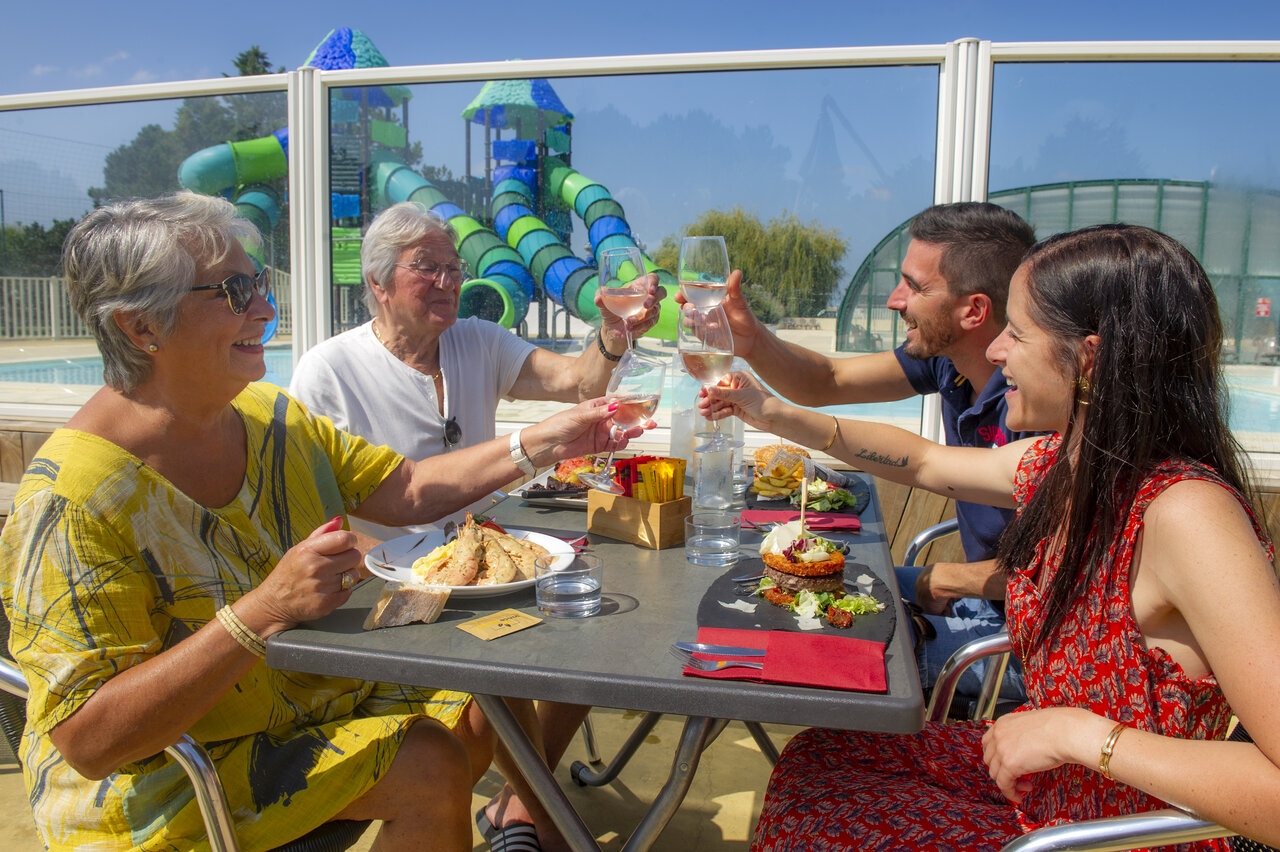 Familia brindando en terraza, piscina y toboganes en el camping CAPFUN Celeste en Breuillet (17).