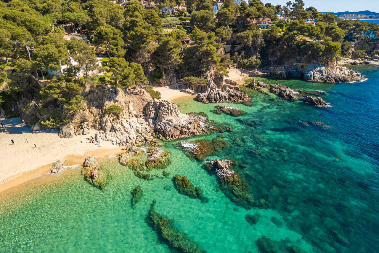 Playa de arena fina, calas rocosas y mar turquesa en el camping CAPFUN Treumal.