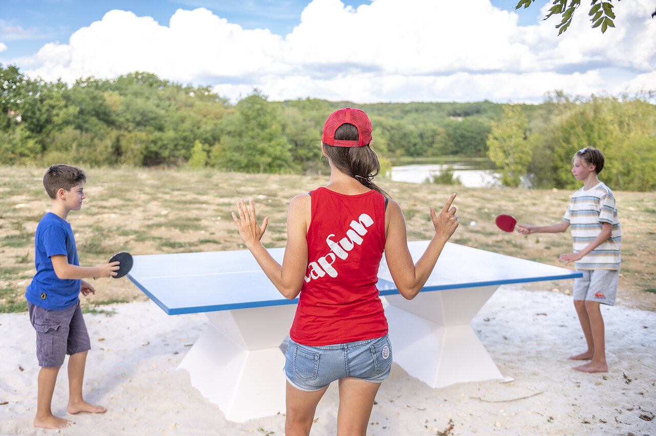 Familia jugando al ping-pong en mesa exterior en el camping CAPFUN Ullule en Tournon d'Agenais (47).