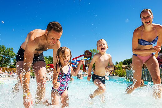 Familia feliz jugando en piscina de olas con toboganes en camping CAPFUN Ullule en Tournon d'Agenais (47).