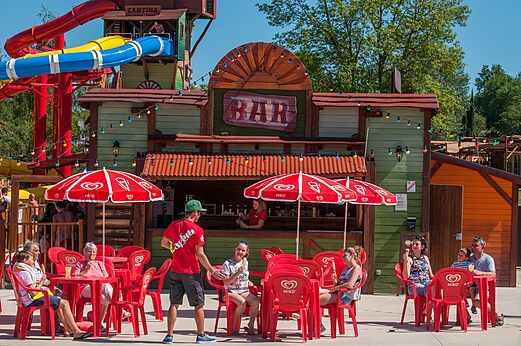 Bar exterior, mesas rojas, sombrillas y toboganes en camping CAPFUN Ullule.