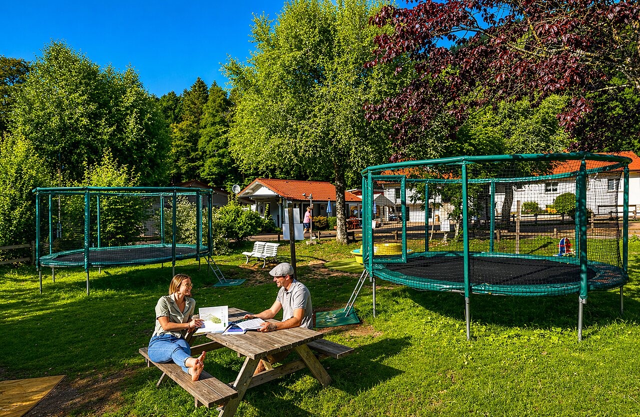 Dos trampolines y pareja en mesa de picnic en el camping CLICOCHIC Verte Vall�e en XONRUPT LONGEMER.