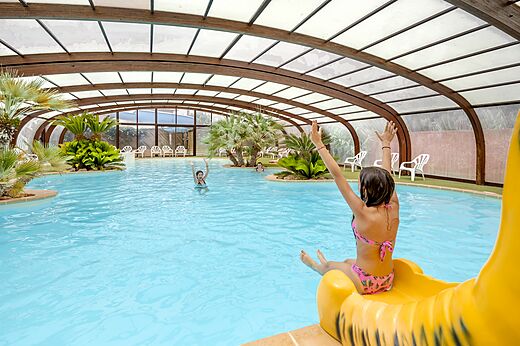 Piscina cubierta con tobogán y niños en el camping CAPFUN Vignes d'Or en Serignan