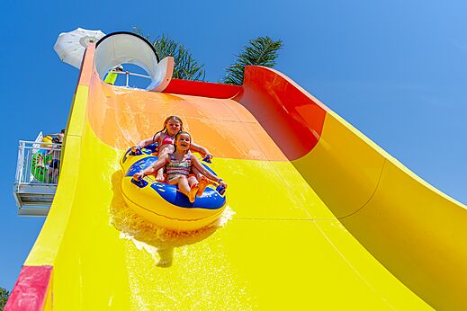 Dos niños en flotador bajan por un tobogán acuático gigante en el camping CAPFUN Vignes d'Or en Serignan.