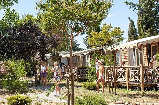 Mobil-homes de madera con terrazas y gente jugando bádminton en el camping CAPFUN Vignes d'Or en Serignan.