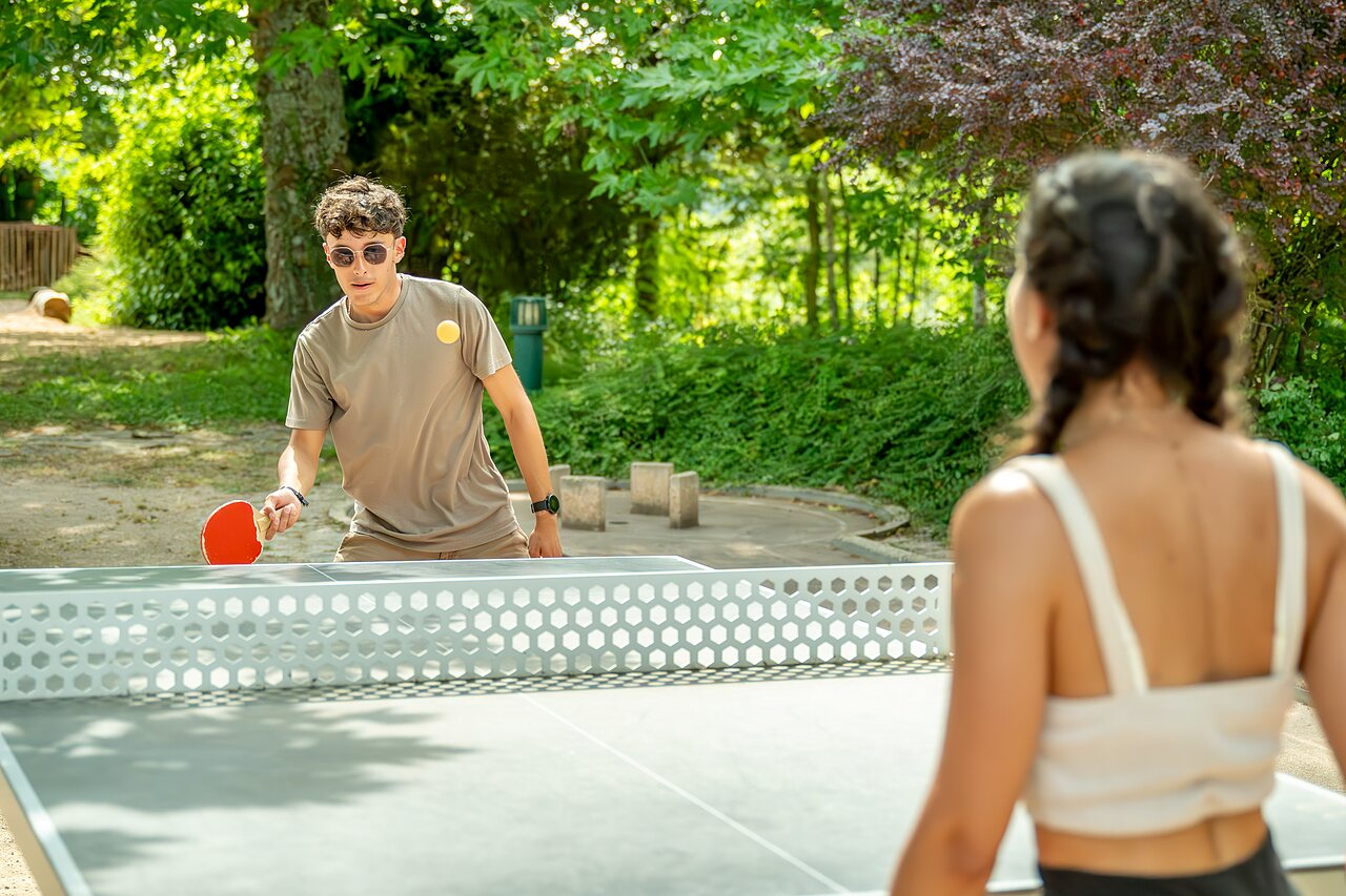J�venes jugando al ping-pong en mesa exterior en el camping CLICOCHIC Village des Meuniers.