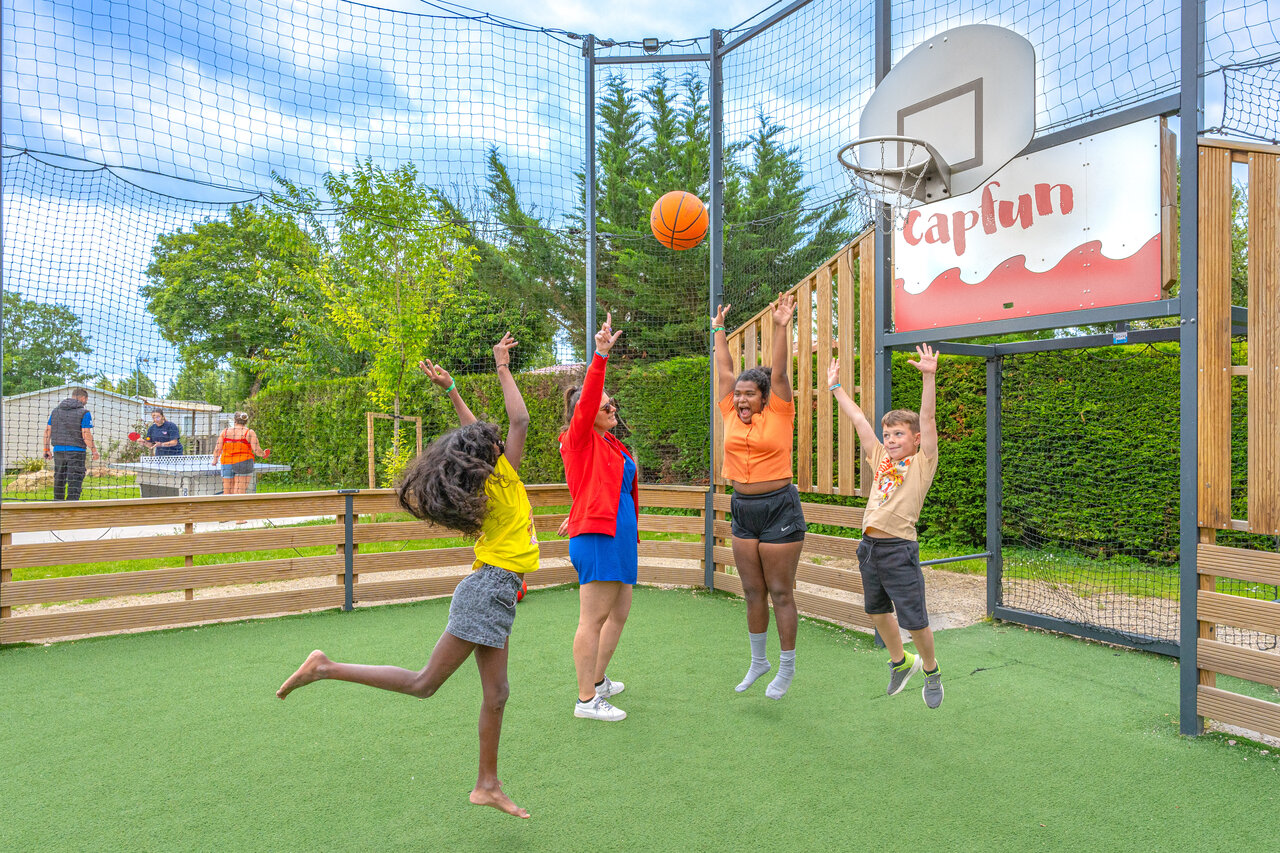Ni�os y adultos jugando baloncesto en cancha multideporte en el camping CAPFUN Le Village Parisien en VARREDDES (77).