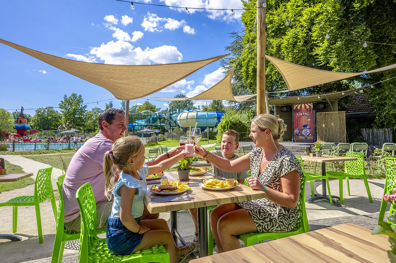 Familia comiendo en terraza, piscina y toboganes en el camping CAPFUN Vlinderloo en Enschede.