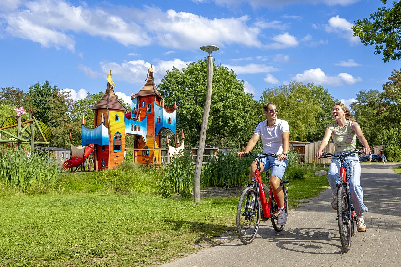 Parque infantil castillo colorido y pareja en bici en el camping CAPFUN Vlinderloo en Enschede.