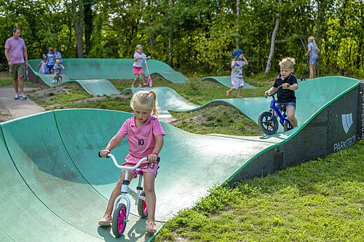 Niños divirtiéndose en la pista de pump track en bicicleta en el camping CAPFUN Vlinderloo en Enschede.