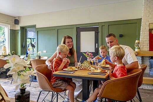 Familia sonriente disfrutando una comida en el restaurante del camping CAPFUN Vlinderloo en Enschede.