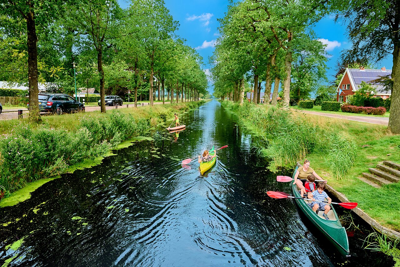 Familia en canoa y paddleboard en el canal arbolado del camping CAPFUN De Waldsang en Bakkeveen.