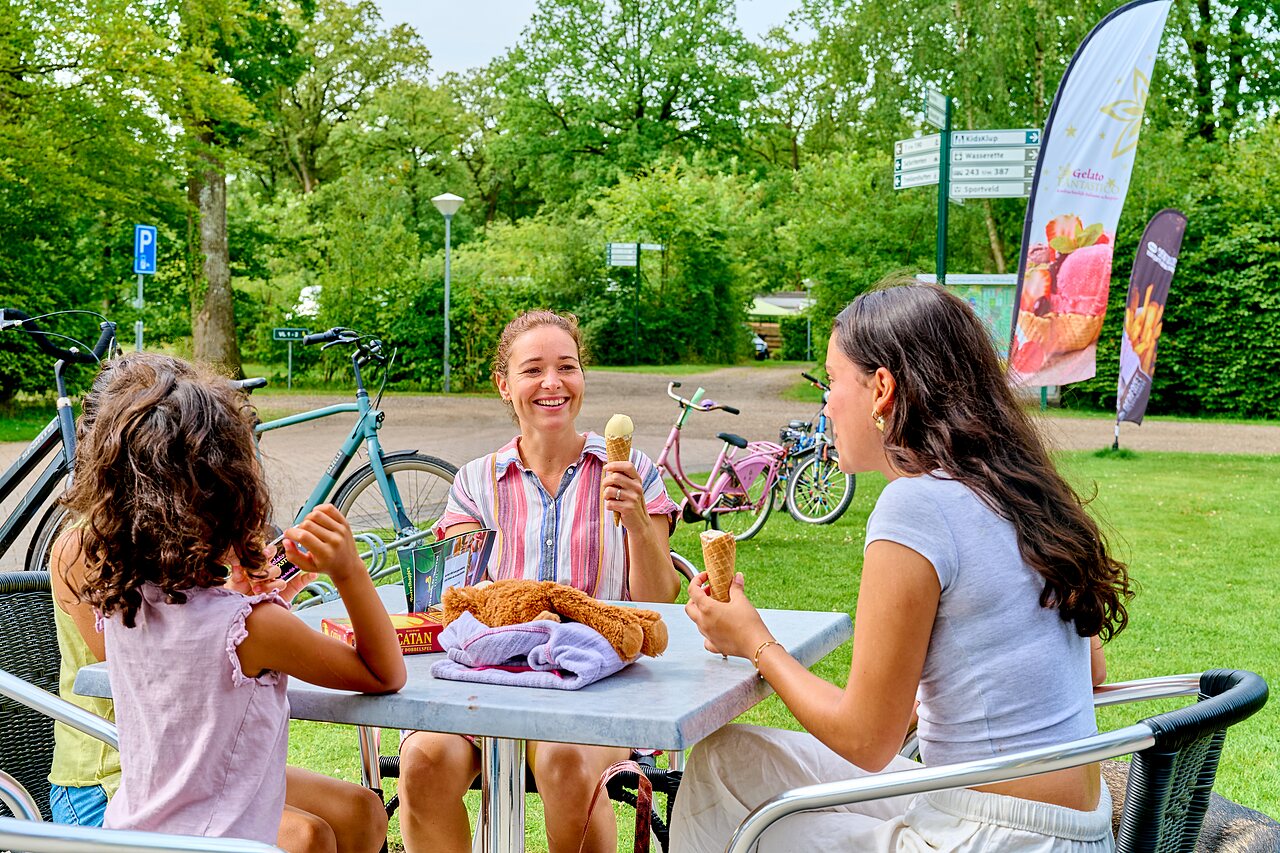 Familia sonriente disfrutando helados en terraza, bicicletas, en el camping CAPFUN De Waldsang en Bakkeveen