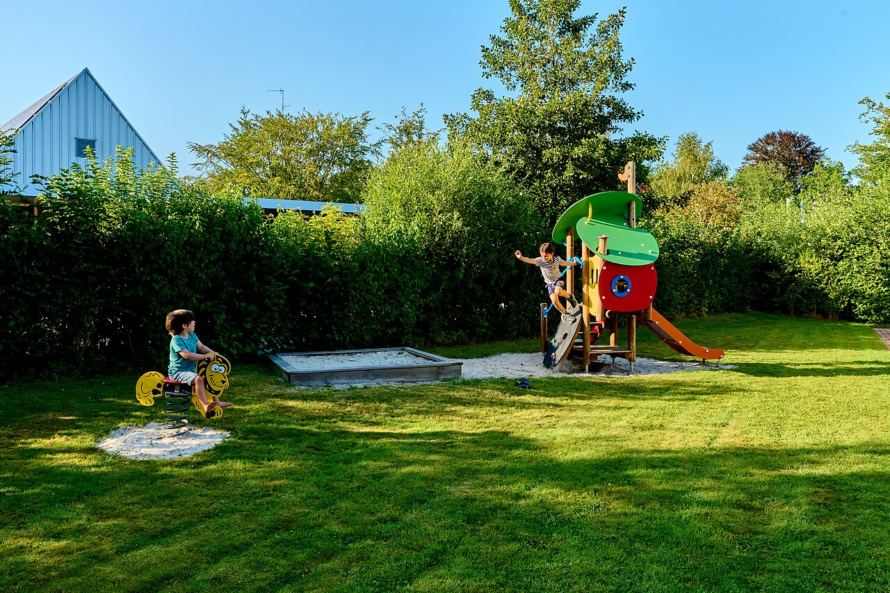 Zona de juegos con tobog�n, estructura para escalar y ni�o en balanc�n en el camping CAPFUN De Waldsang en Bakkeveen.