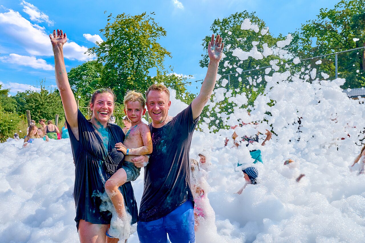 Familia sonriente disfrutando de una divertida fiesta de espuma en el camping CAPFUN Wieskamp en Winterswijk Henxel.