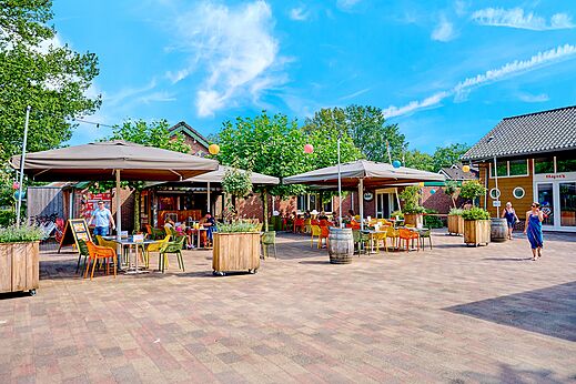 Terraza exterior del restaurante con mesas y sombrillas en el camping CAPFUN Wieskamp.
