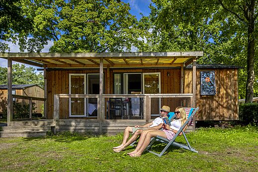 Pareja relajándose frente a un Mobil-home con terraza en el camping CAPFUN de Wondermolen en Molenschot.