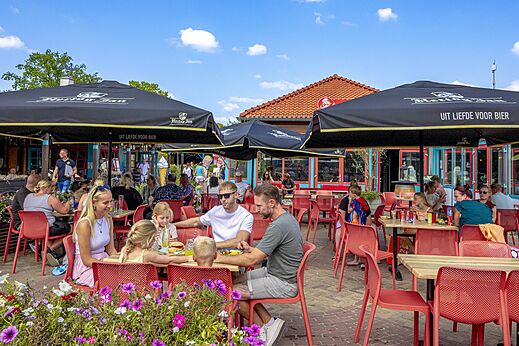 Animada terraza de restaurante con familias y sombrillas en camping CAPFUN Wondermolen Molenschot.