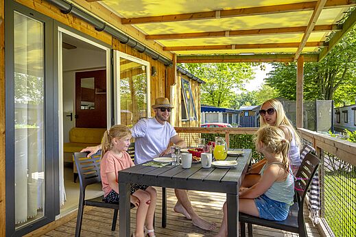 Familia desayunando en la terraza cubierta de un Mobil-home en el camping CAPFUN de Wondermolen en Molenschot.