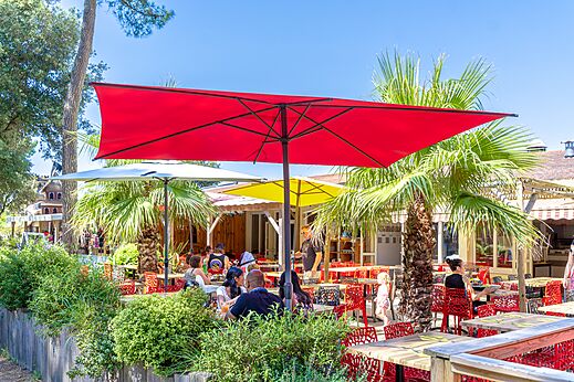 Terraza de restaurante exterior con sombrillas de colores y clientes en el camping CAPFUN Zagarella en LONGEVILLE SUR MER (85).