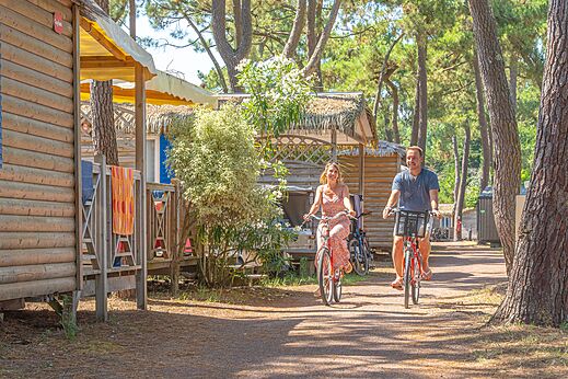 Pareja en bicicleta por camino entre Mobil-homes en bosque en el camping CAPFUN Zephir en Les Mathes La Palmyre (17).