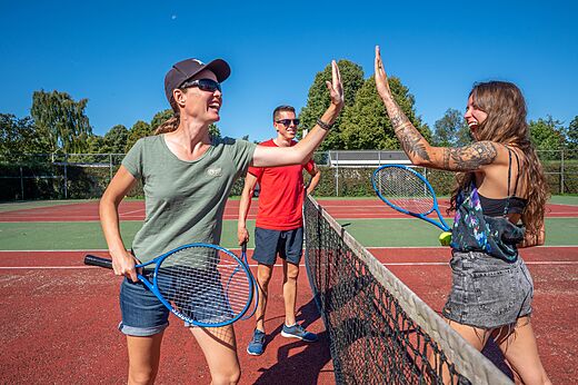 Jugadores de tenis chocando las cinco en la cancha del camping CAPFUN Zeumersehof en Voorthuizen.
